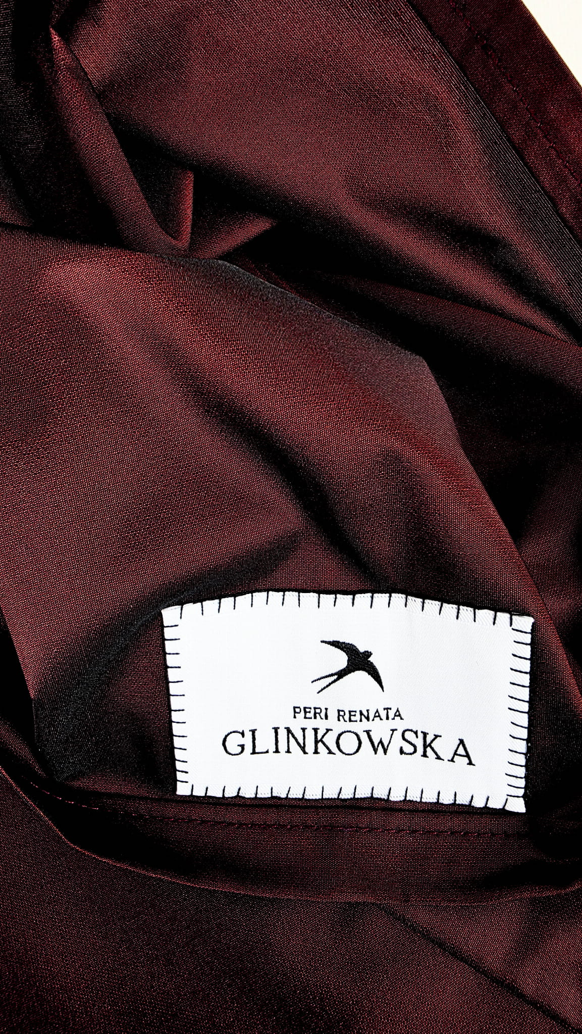 Close-up of burgundy taffeta fabric with the PERI Renata Glinkowska brand label and stitched edge.