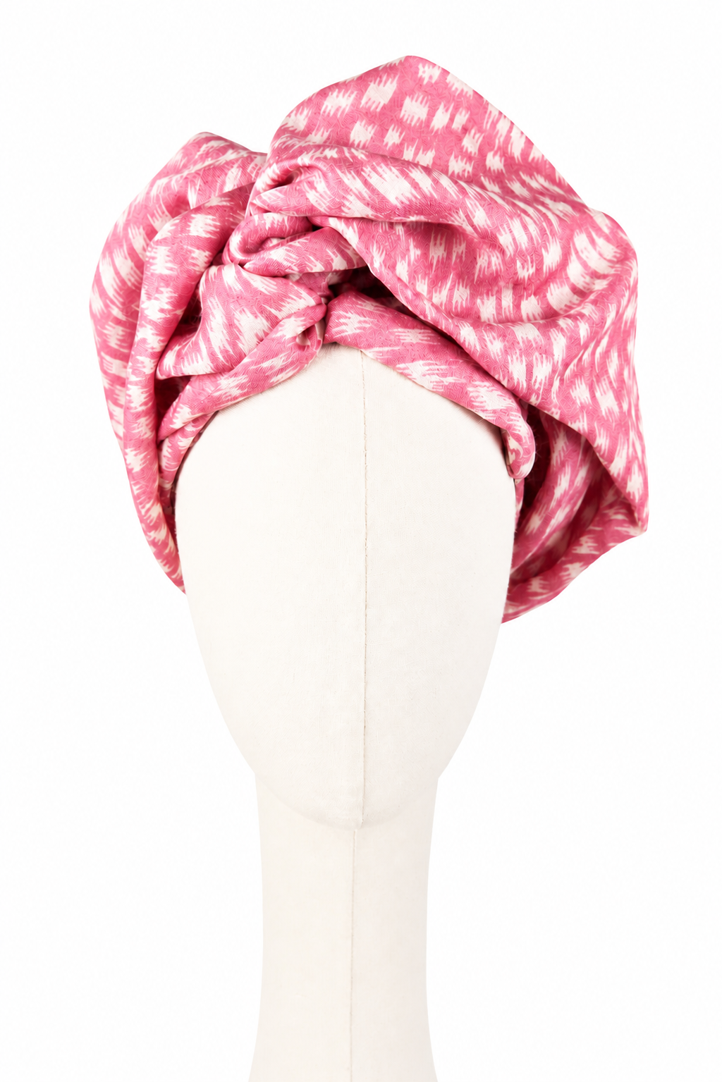 Różowy turban damski Twist Long z pashminy i jedwabiu, pokazany od przodu na kremowym manekinie bez rysów twarzy. Turban jest wysoko i obficie udrapowany w miękkie, asymetryczne fałdy. Malinoworóżową tkaninę pokrywa nieregularny biały nadruk przypominający krótkie pociągnięcia pędzla i cętki. Jasne, jednolite tło.