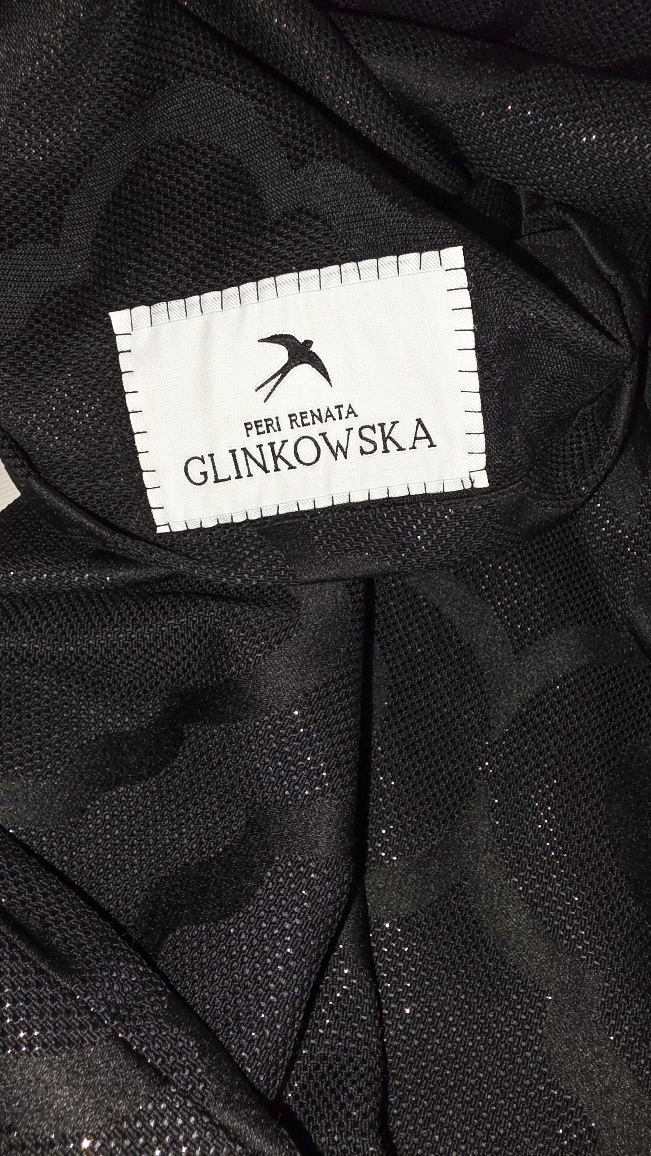 Zbliżenie wnętrza czarnego turbanu z żakardowej tkaniny. Na materiale widoczna jest prostokątna biała metka marki z czarną grafiką jaskółki oraz napisami PERI RENATA i GLINKOWSKA. Wokół metki widać duży ornamentowy wzór tkany w czerni. Różnica między matowymi i połyskującymi nićmi tworzy delikatną grę światła na powierzchni.