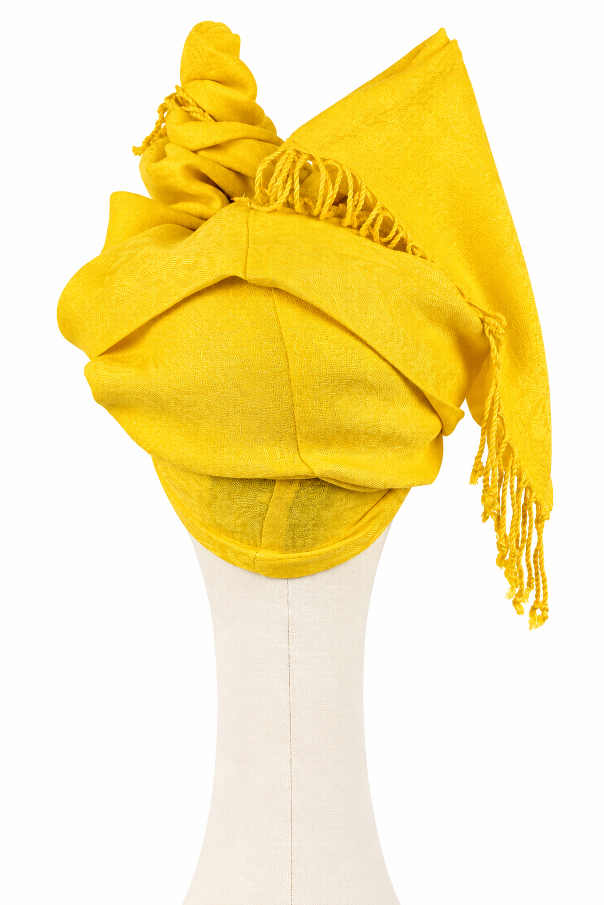 Rear view of a yellow jacquard twist turban with sculptural folds and long fringed ends.