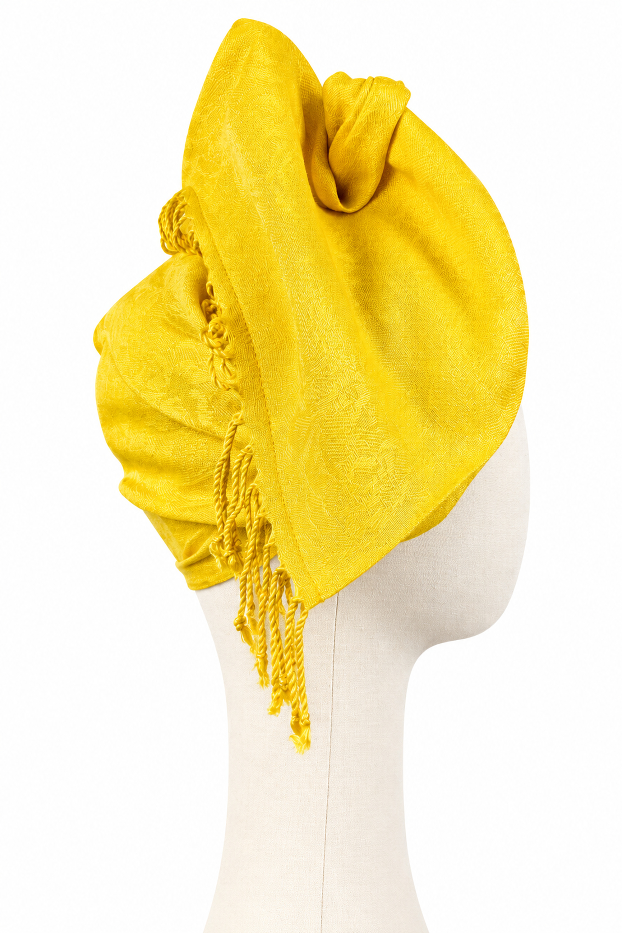 Yellow jacquard twist turban with decorative fringes, shown from the side on a fabric mannequin.