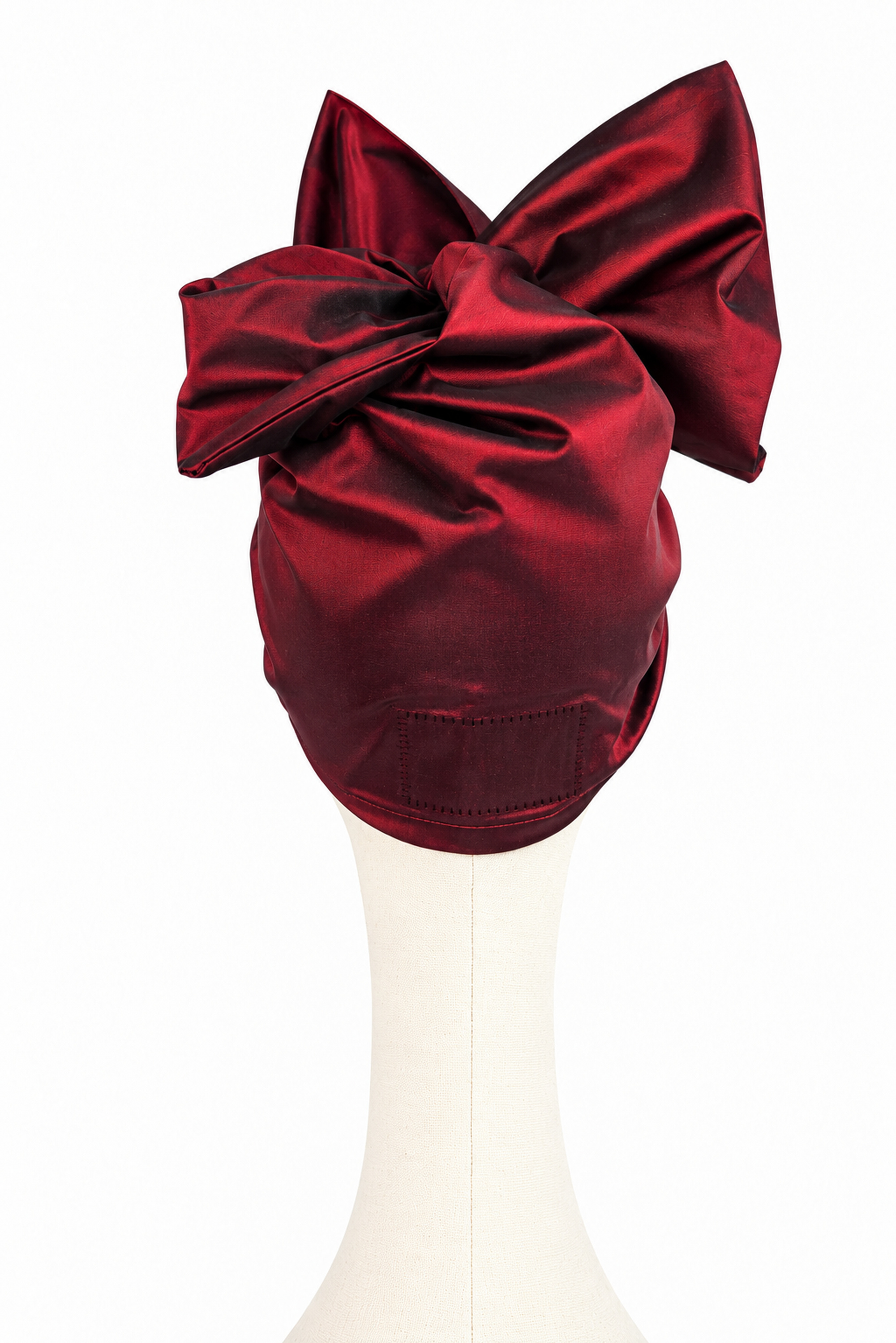 Rear view of a women’s short burgundy taffeta Twist evening turban showing its folds and bow construction.