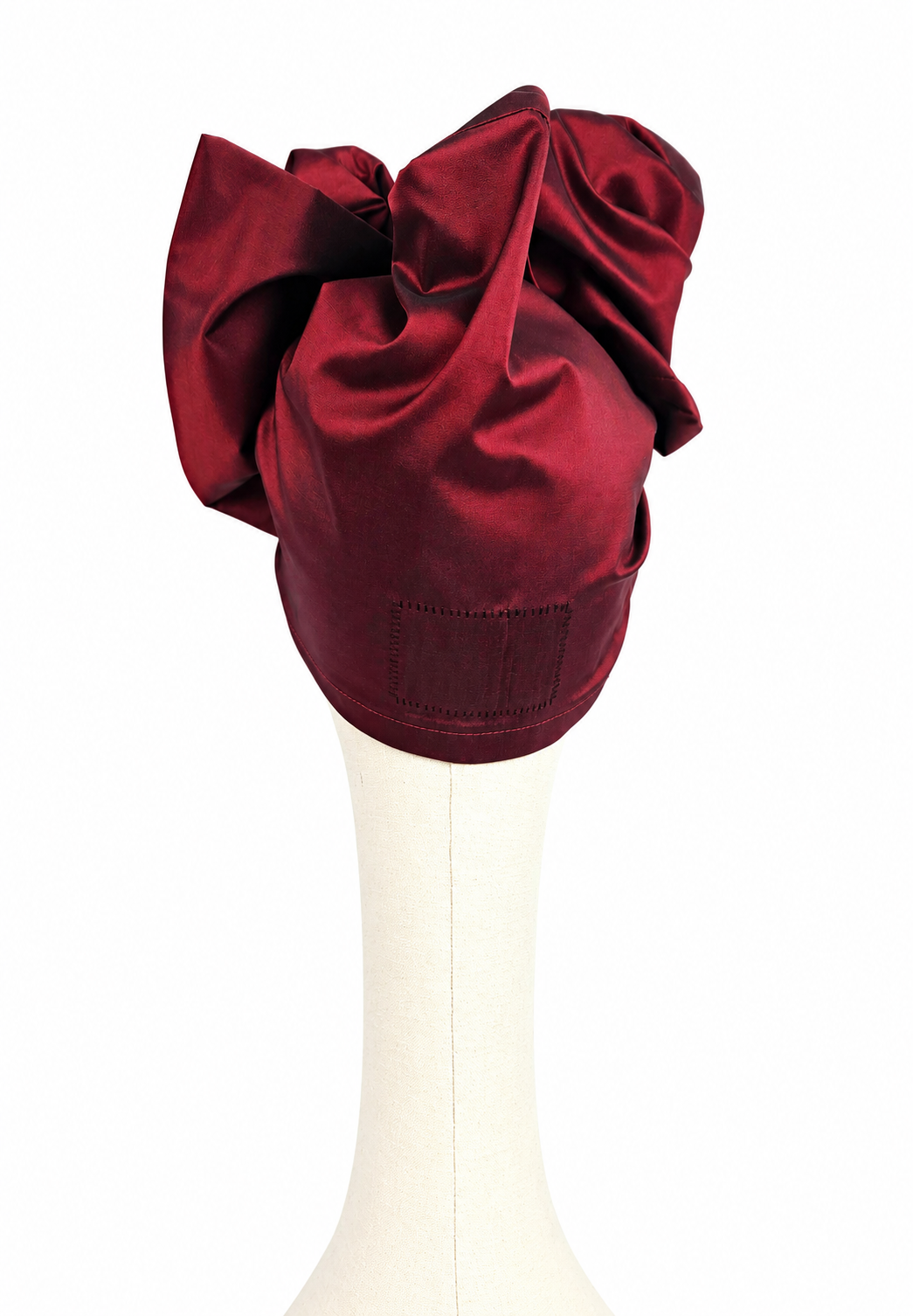 Rear view of a women’s long burgundy taffeta Twist evening turban showing layered folds and stitched detailing.