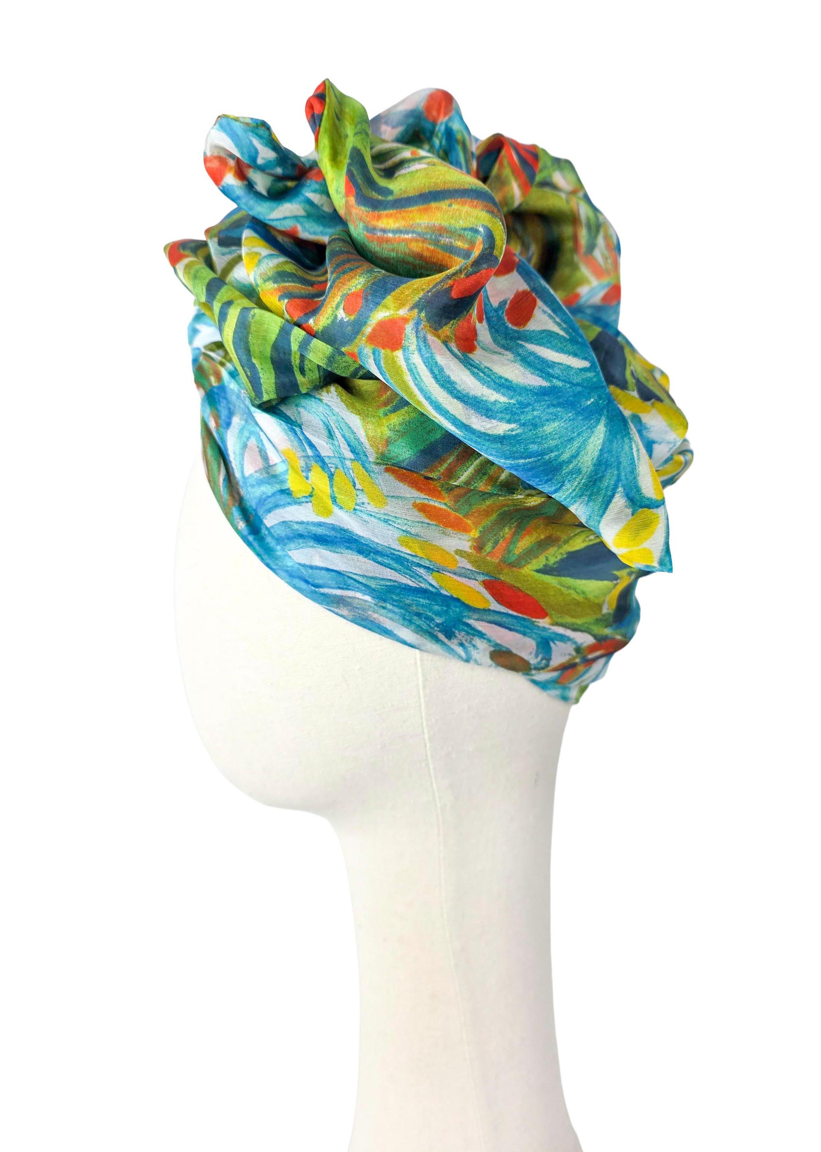 Turban z jedwabiu z boku. Widać wysoką, drapowaną górę i gładką opaskę wokół głowy. Przeważają limonkowa zieleń i turkus z pomarańczowymi akcentami.