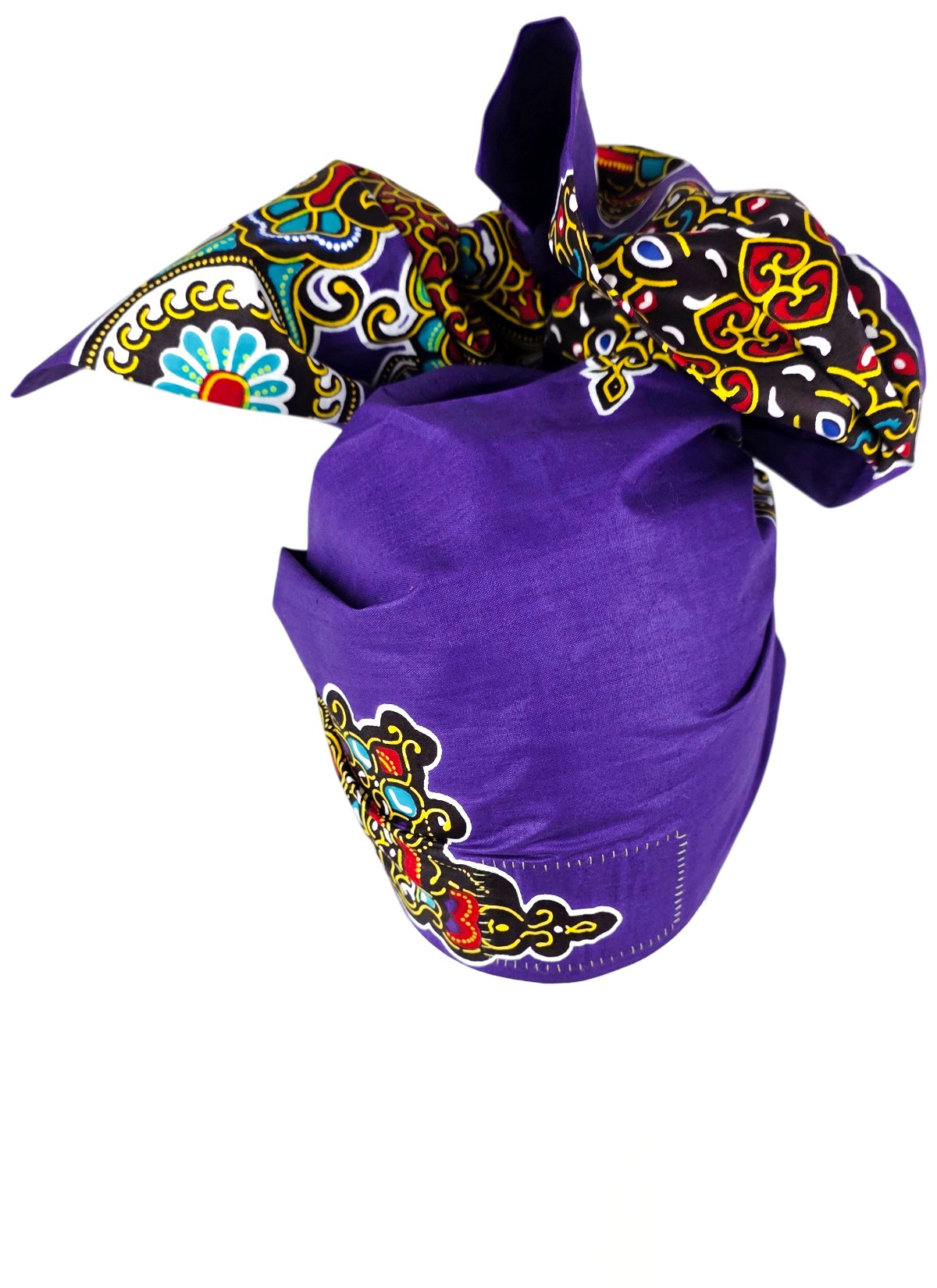 Back view of a purple cotton Twist Long turban with a large bow in black, red, yellow and turquoise ornamental print, on a mannequin.