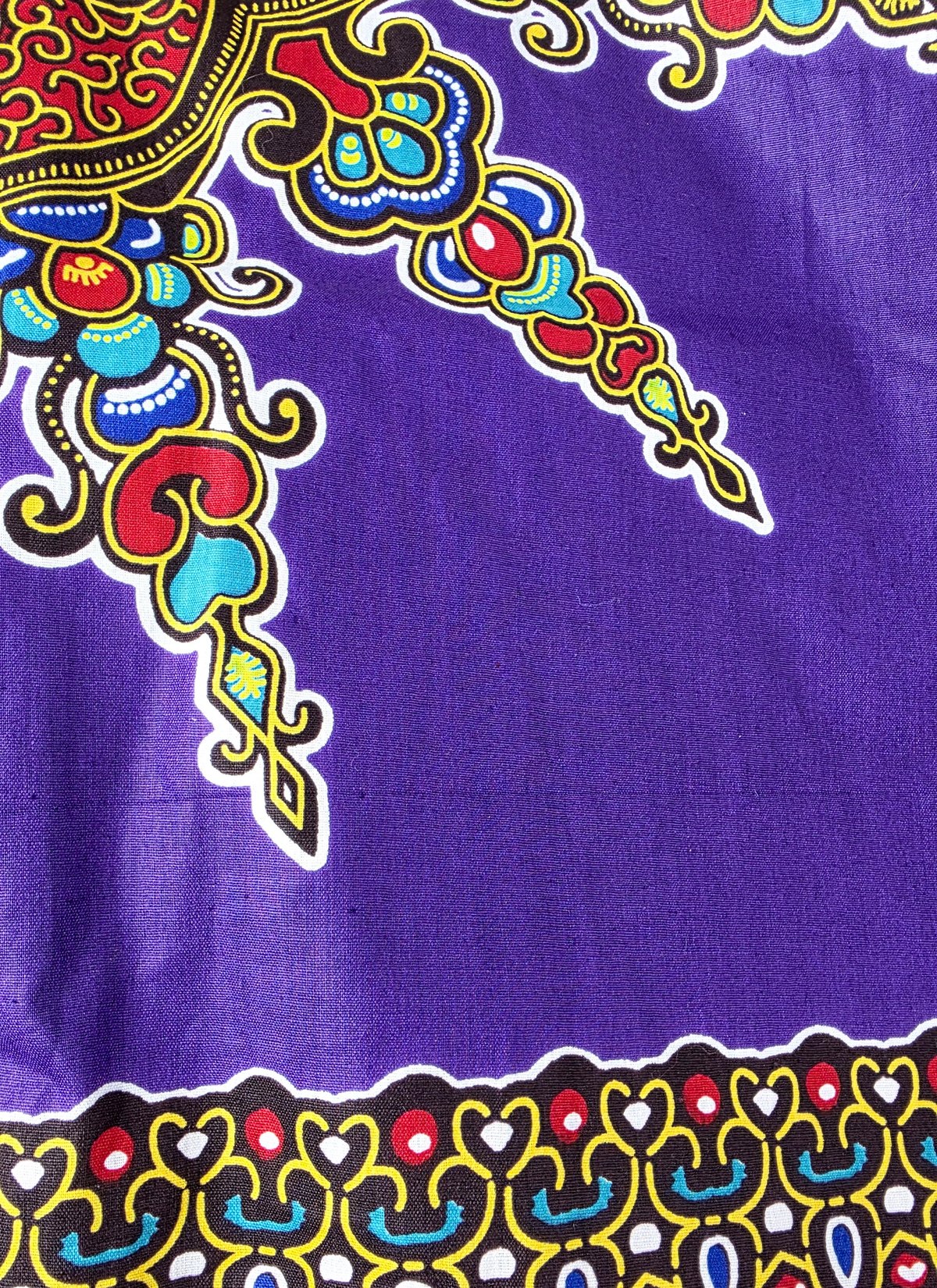 Close-up of purple African cotton fabric with a large red, turquoise, yellow and blue ornament and a black patterned border.