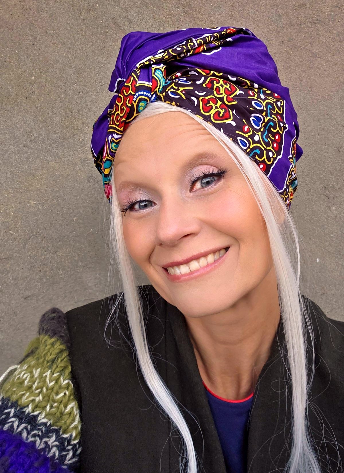 Smiling woman wearing a purple Twist Long turban with a multicolor African ornament wrapped as a full head covering.