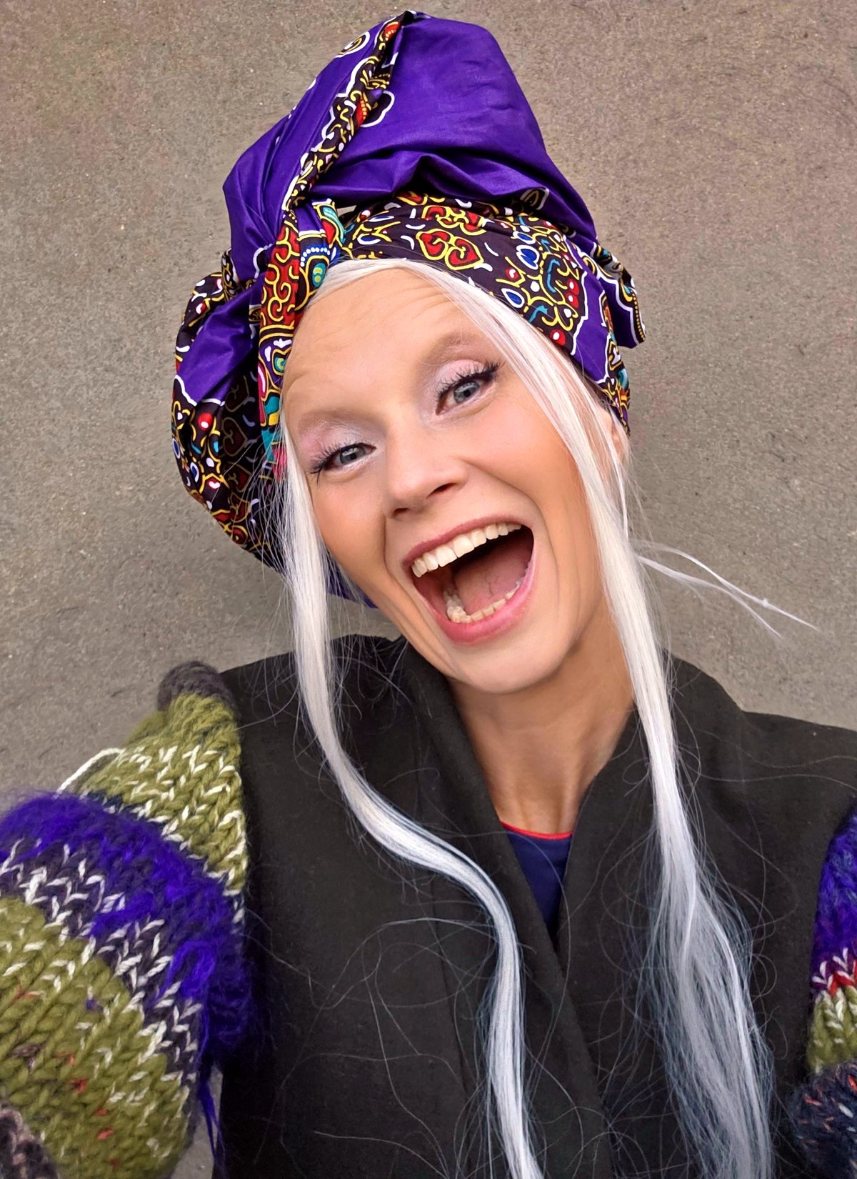 Laughing woman in a colorful knitted cardigan wearing a voluminous purple African print turban sewn in a Polish artist's studio.