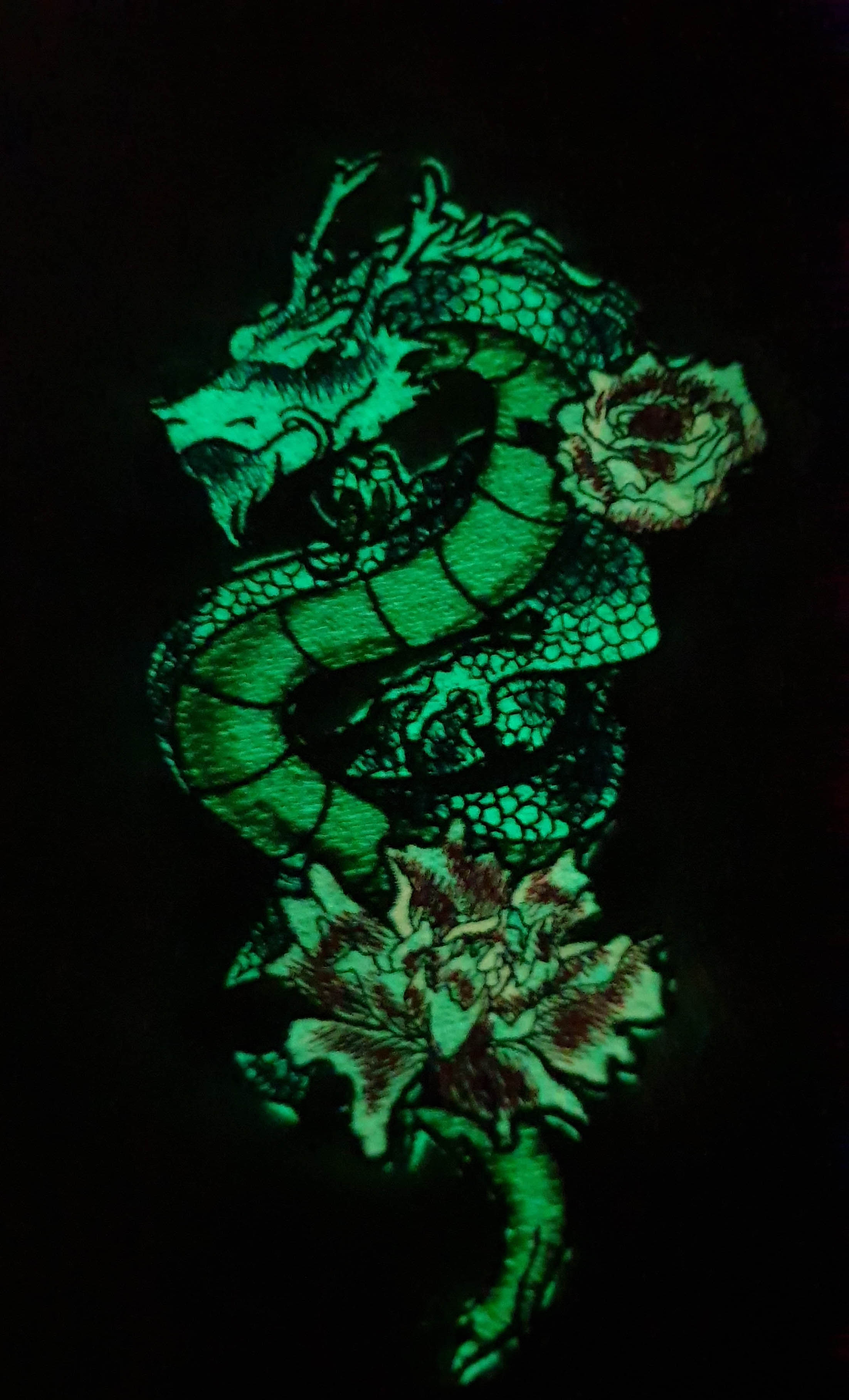 Embroidered dragon with flowers on the knitted sweater glowing green in the dark.