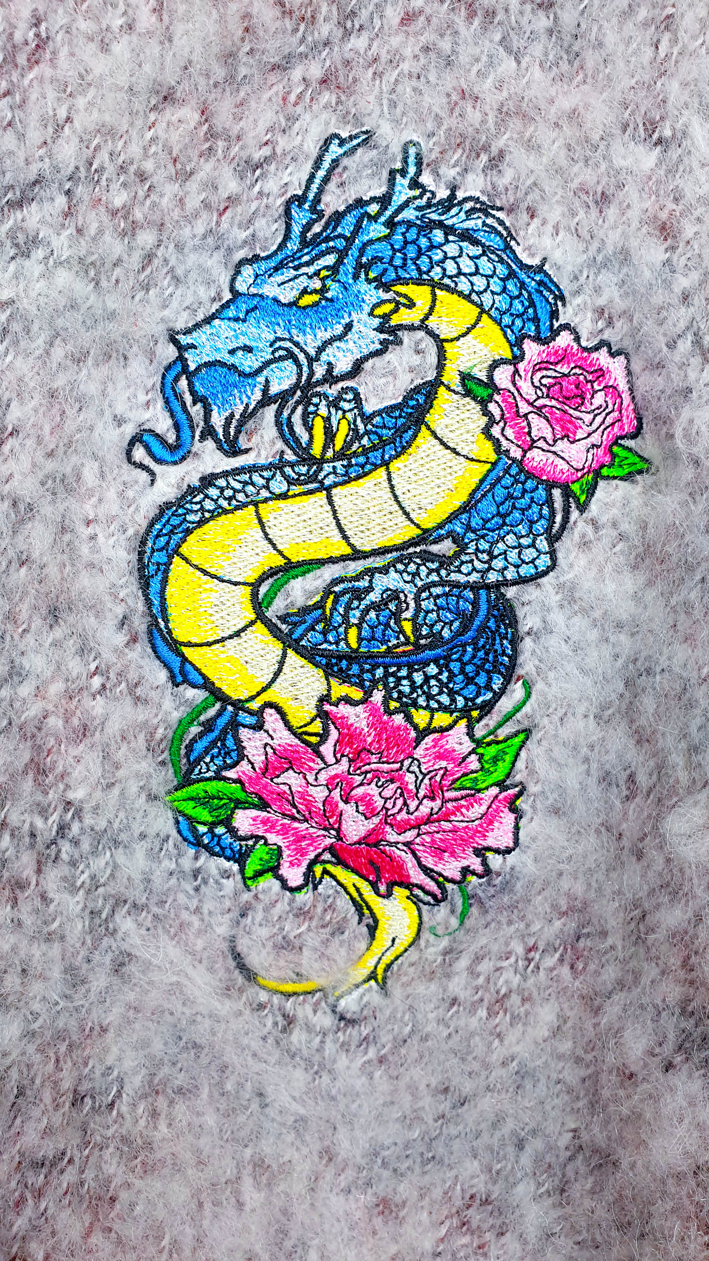Close-up of the embroidered blue and yellow dragon with pink peonies on fluffy melange knit.