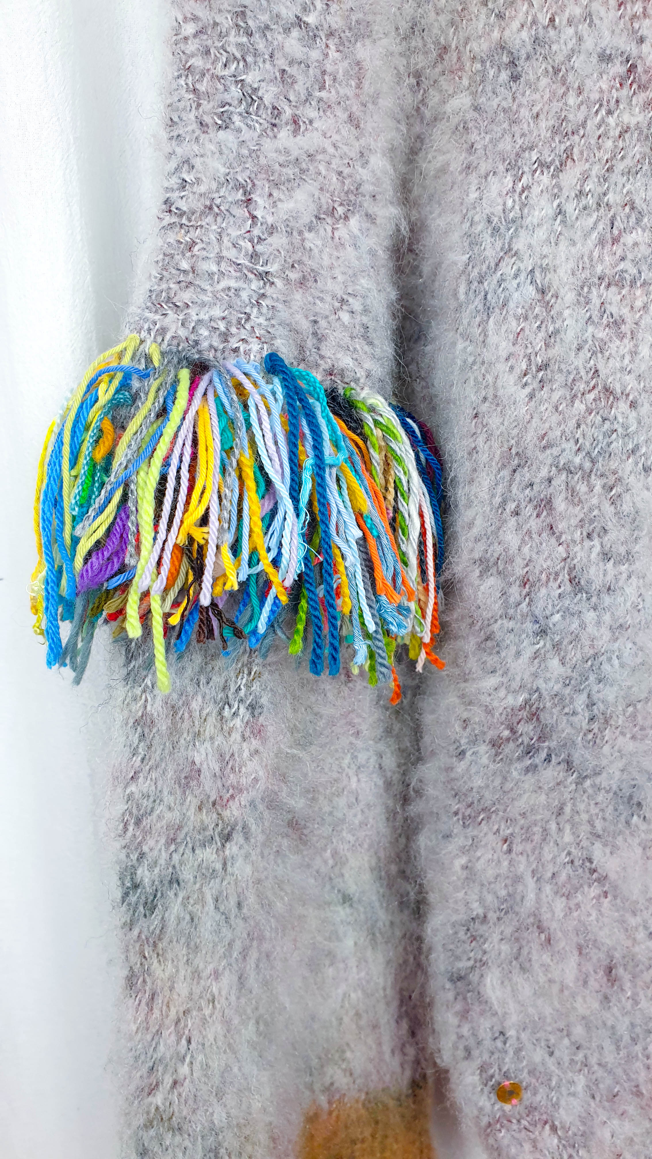 Close-up of multicolor yarn fringe on the sleeve of a fluffy gray knitted sweater.