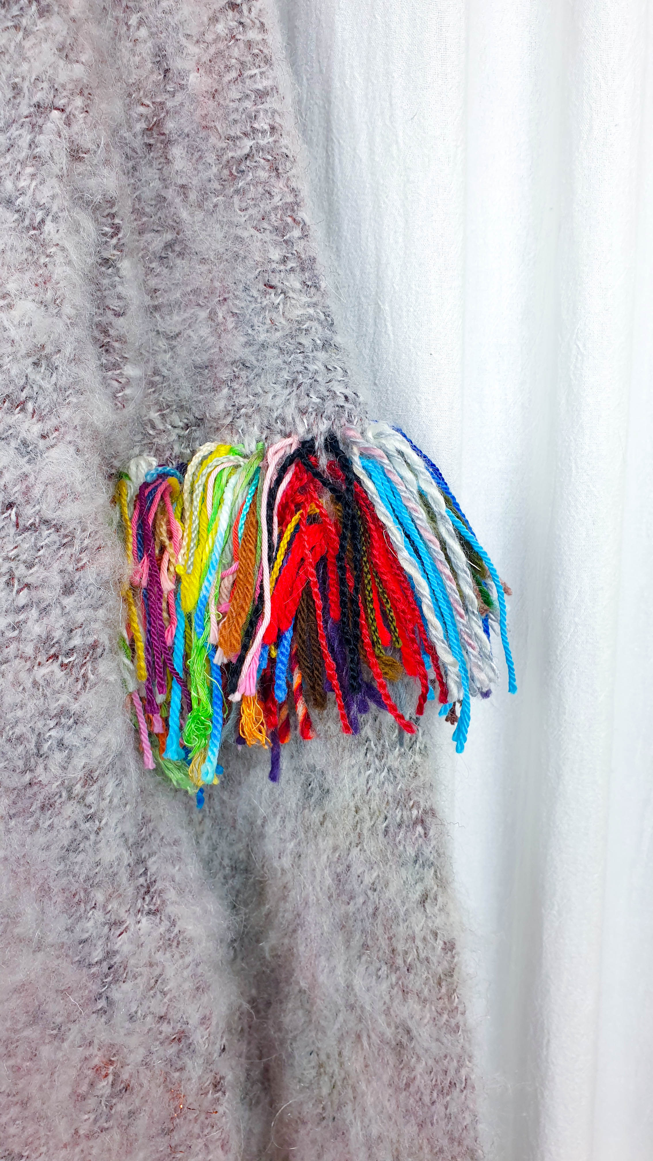 Colorful fringe made from reclaimed yarn sample ends on the sleeve of a fluffy knitted sweater.
